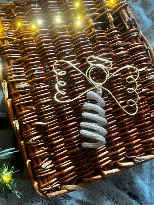 A handmade angel tree topper made in gold wire and cream sparkly knit yarn placed on a brown wicker basket, with Christmas tree lights shining on it.