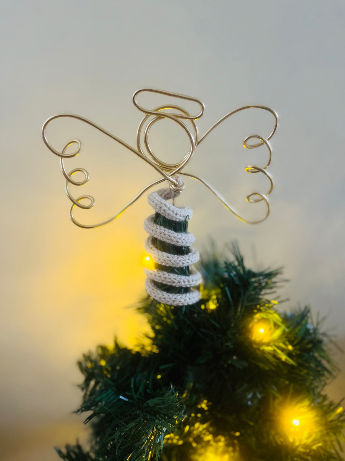 A handmade wire angel tree topper on top of of a Christmas tree